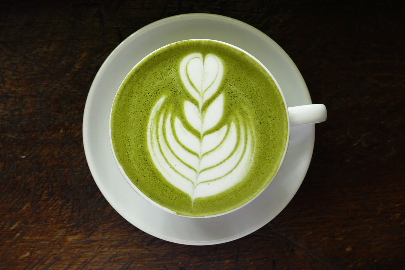 A matcha latte in a white cup, with a leaf design in the froth. 