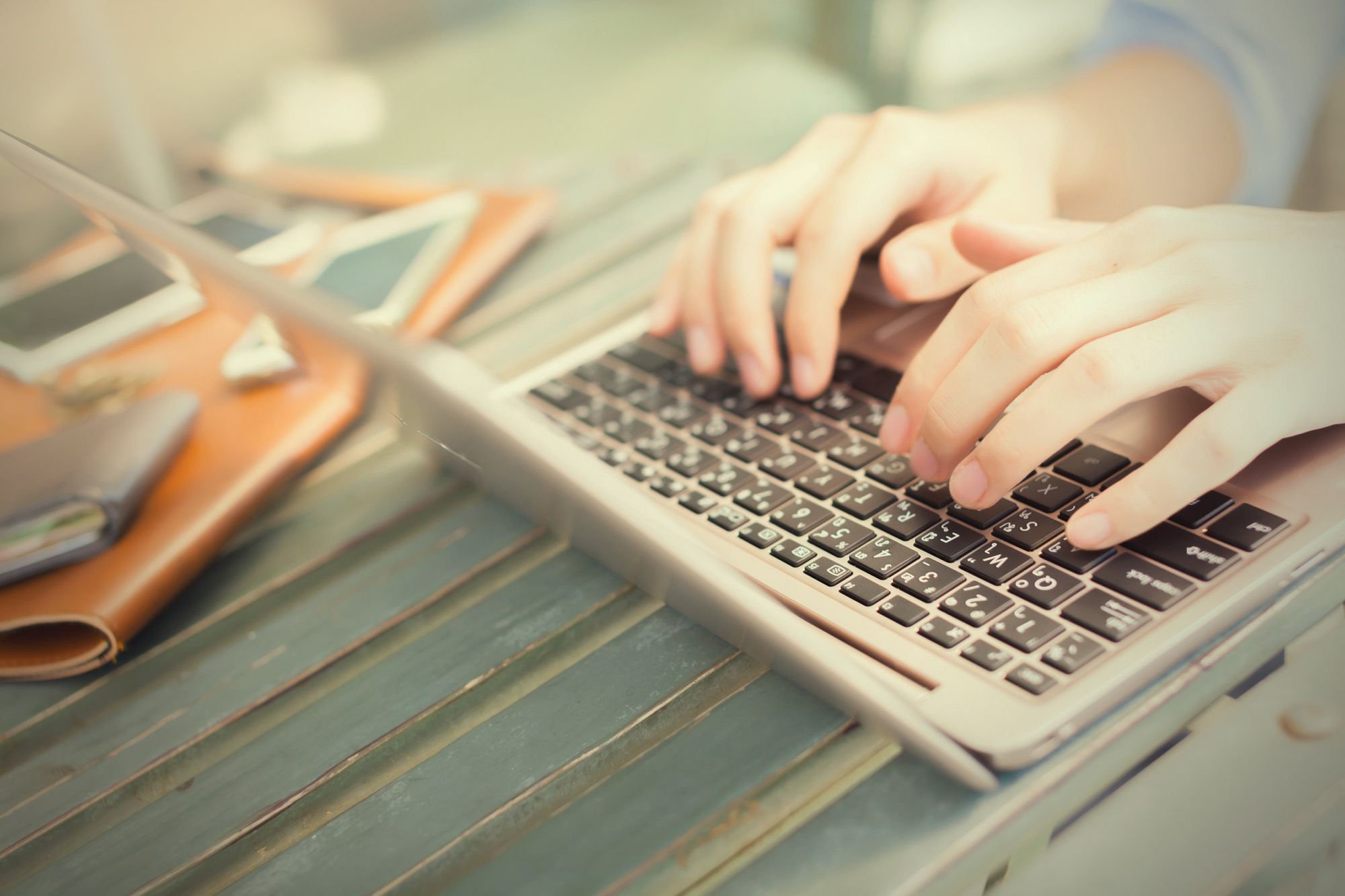 Hands typing at a laptop at an outdoor table.