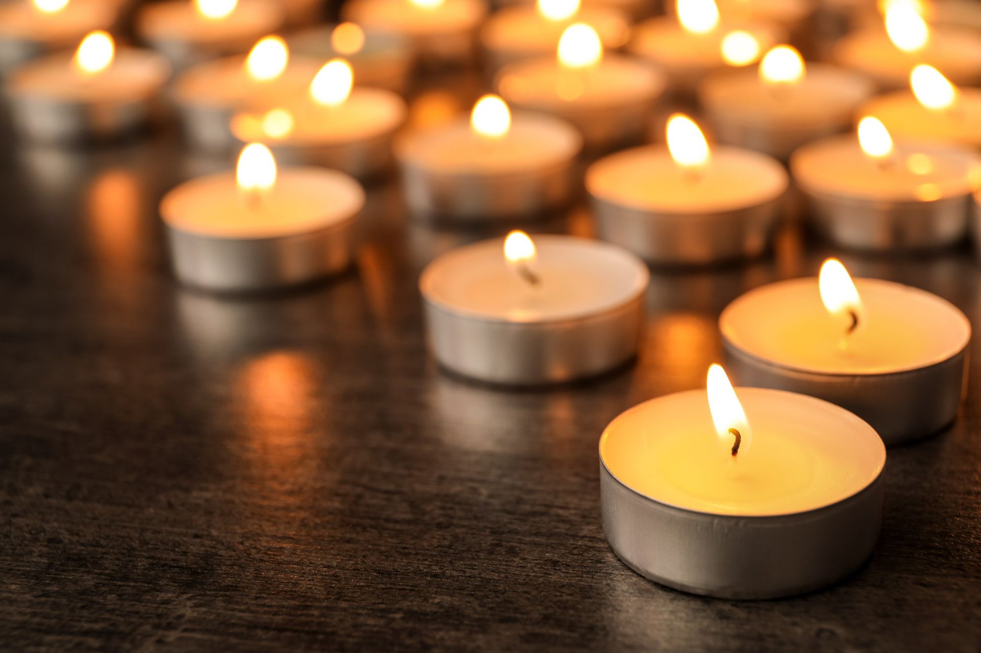 Tealight candles on a wooden surface. They are all lit. The focus is on the candle in the front. 