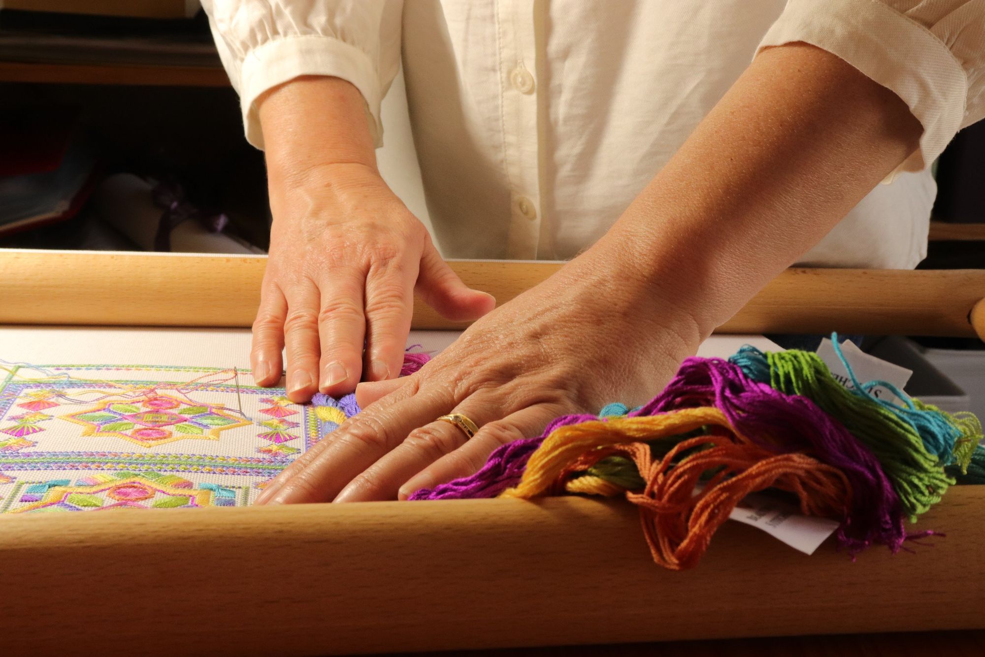 Ann-Marie's hands, an embroidery canvas and different coloured threads. 