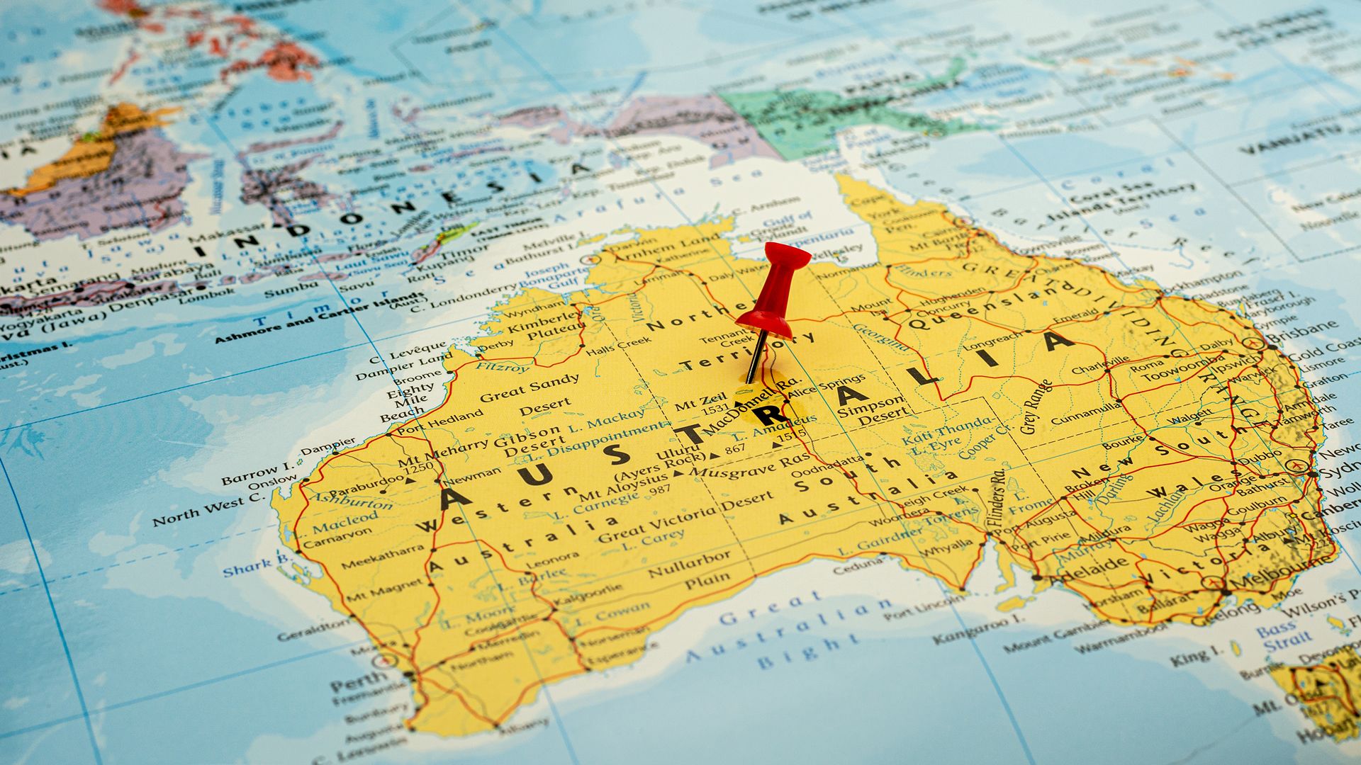 A map of Australia with a red thumb tack pressed into the middle of it. 