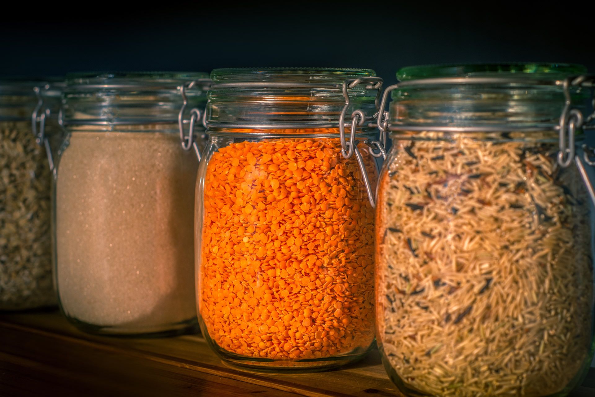 Several glass jars with grains like rice and lentils on a shelf. 