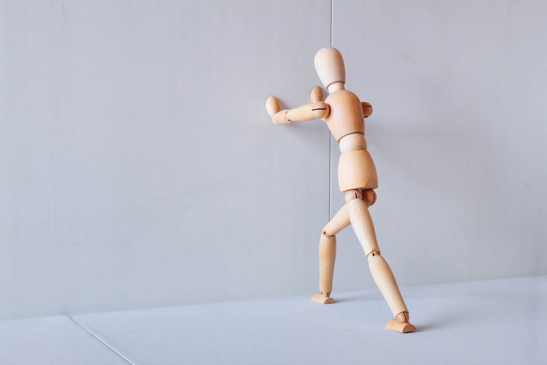 A wooden figure pushes against a wall.