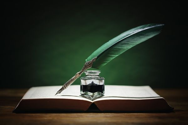 An old-fashioned quill pen and ink on top of an old book. 