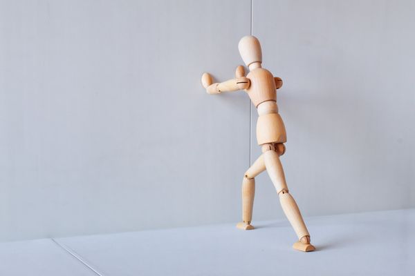 A wooden figure pushes against a wall. 